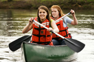 Two girls in life jackets canoeing.